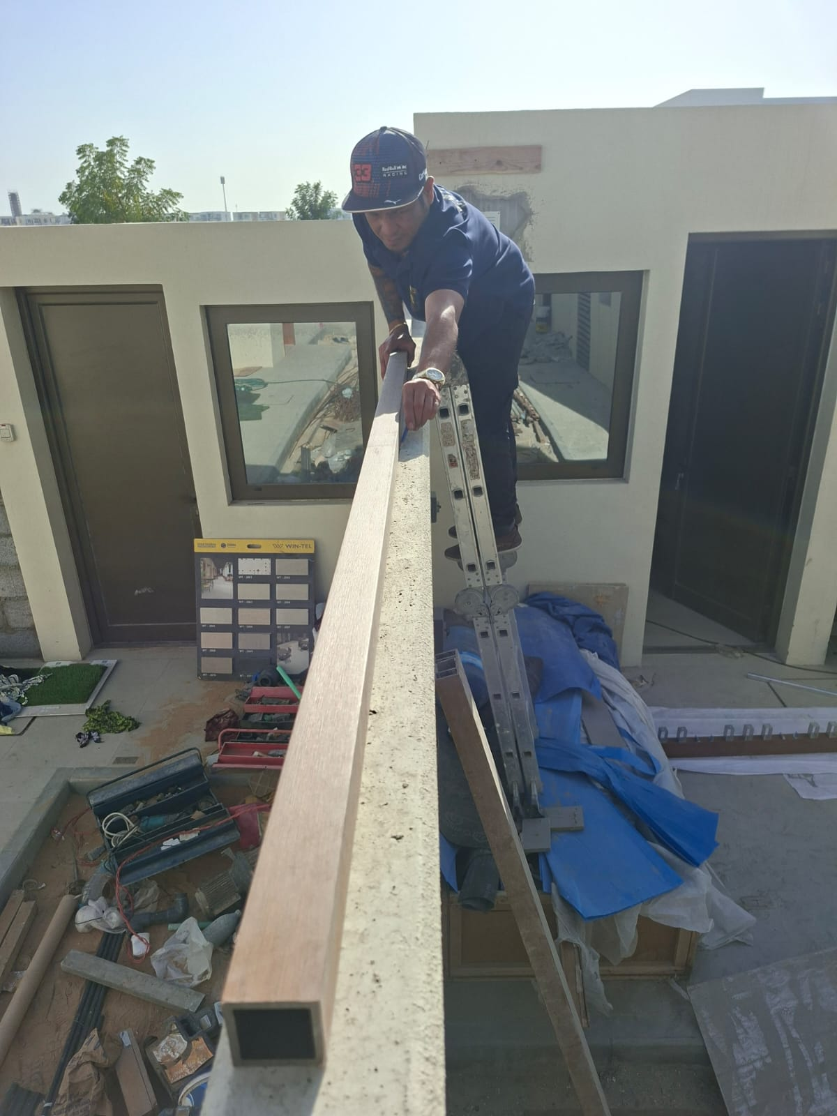 Carpenter drilling brackets onto composite timber posts for the rooftop pergola build