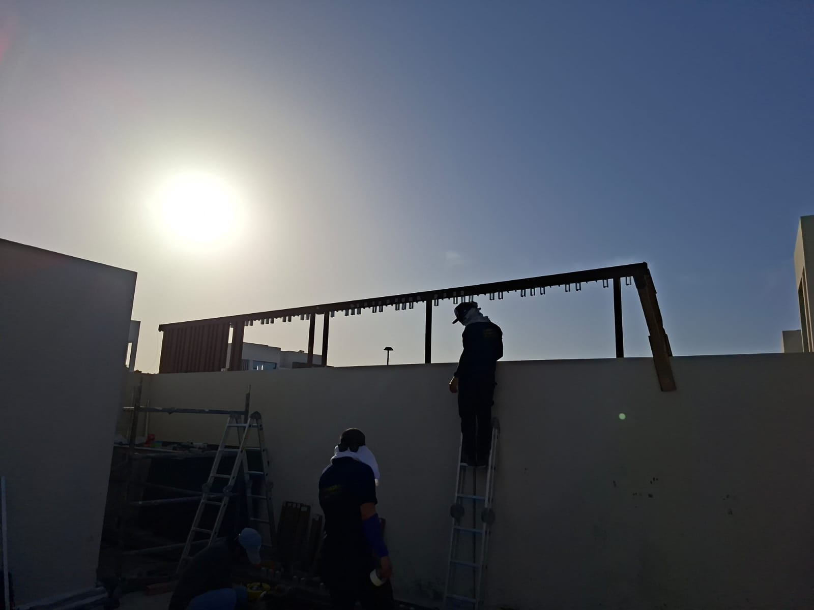 Silhouetted crew fixing the pergola steel frame at golden hour on the villa rooftop