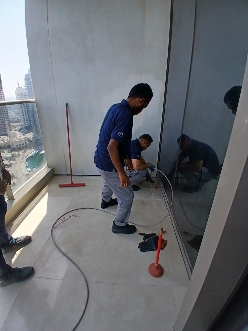 Two-man team clearing a blocked balcony drain in a high-rise apartment