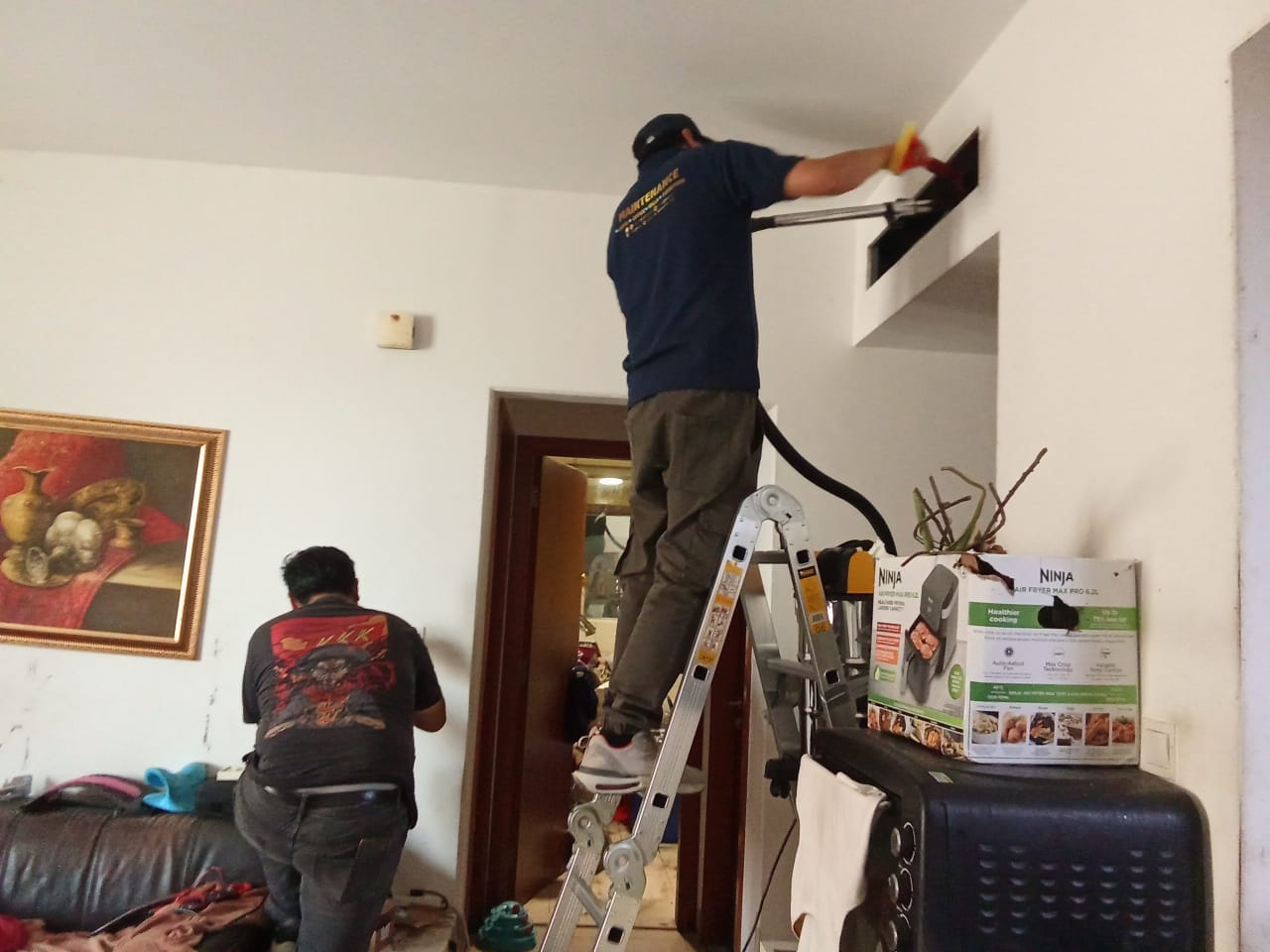Vacuuming and cleaning a high-level AC vent from a ladder